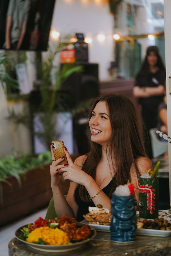 Smiling woman using a smartphone at a restaurant table with food.